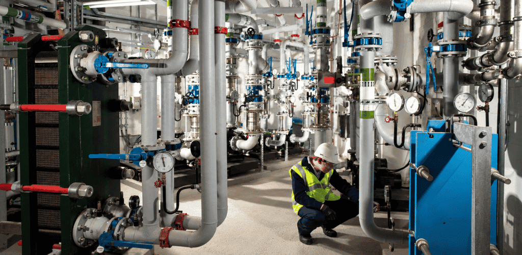 Engineer carrying out planned maintenance in a commercial plant room with industrial pipework and equipment.