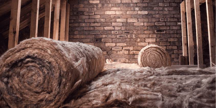 Close-up of loft insulation rolls beneath exposed timber framing and brickwork during a UK home retrofit.